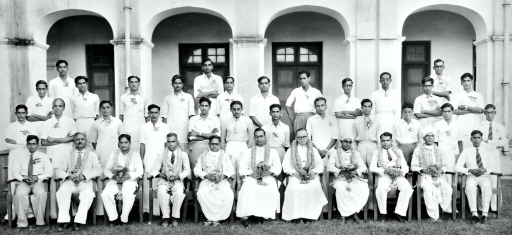 Group photo of the 1953 batch of BA Honours in mathematics with Fr. Racine, seated seventh from the left. M.S. Narasimhan is standing in topmost row on the left and C.S. Seshadri is standing just above Fr. Racine on the left.